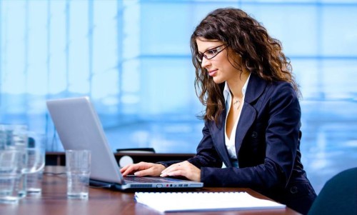 Дівчина в окулярах сидить за столом навпроти ноутбука і шукає інформацію в інтернеті