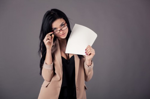 Дівчина в окулярах тримає в руці аркуші паперу, на якому хоче записати список ідей без вкладень