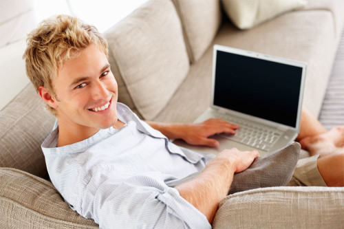 Гарний хлопець сидить на дивані з ноутбуком в руках