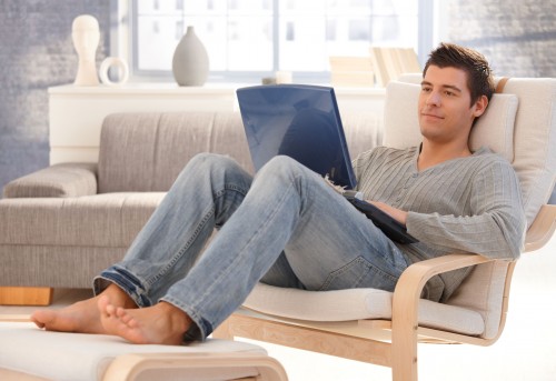 Хлопець сидить на дивані з ноутбуком в руках